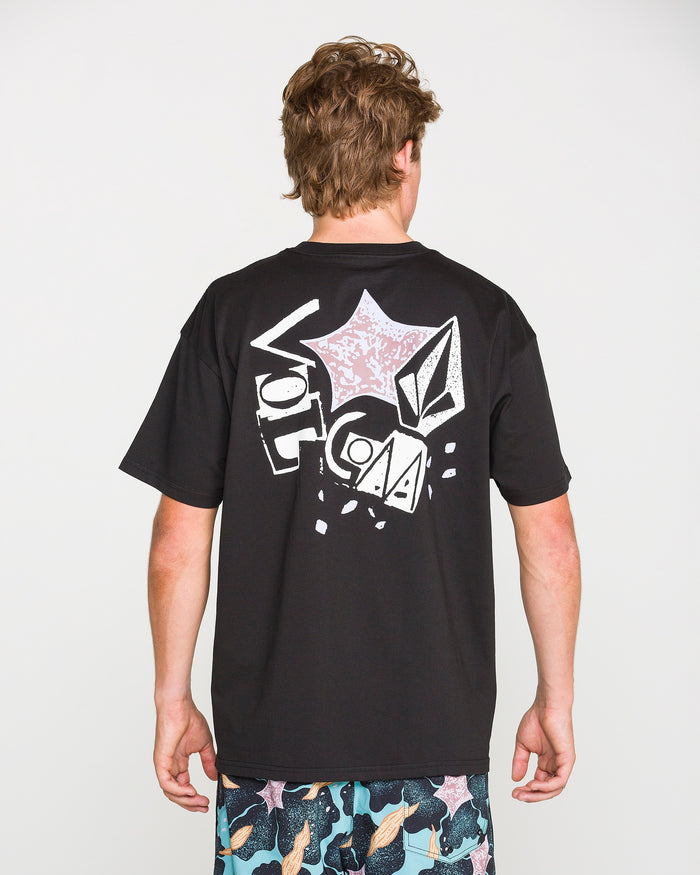 A person with short, light brown hair is seen from behind wearing the Volcom Men's Concrete Jungle Short Sleeve Tee in black—crafted from heavyweight ringspun cotton and showcasing bold graphic designs along with "Volcom" printed on the back. They are also sporting vibrant, patterned shorts.