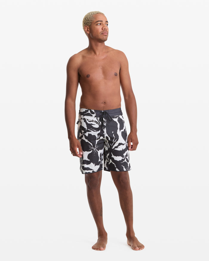A shirtless man with short blond hair stands barefoot against a white background, modeling the Volcom Men's Contact Scallop Stoney 19 swim trunks. He looks slightly to the side with a relaxed posture.