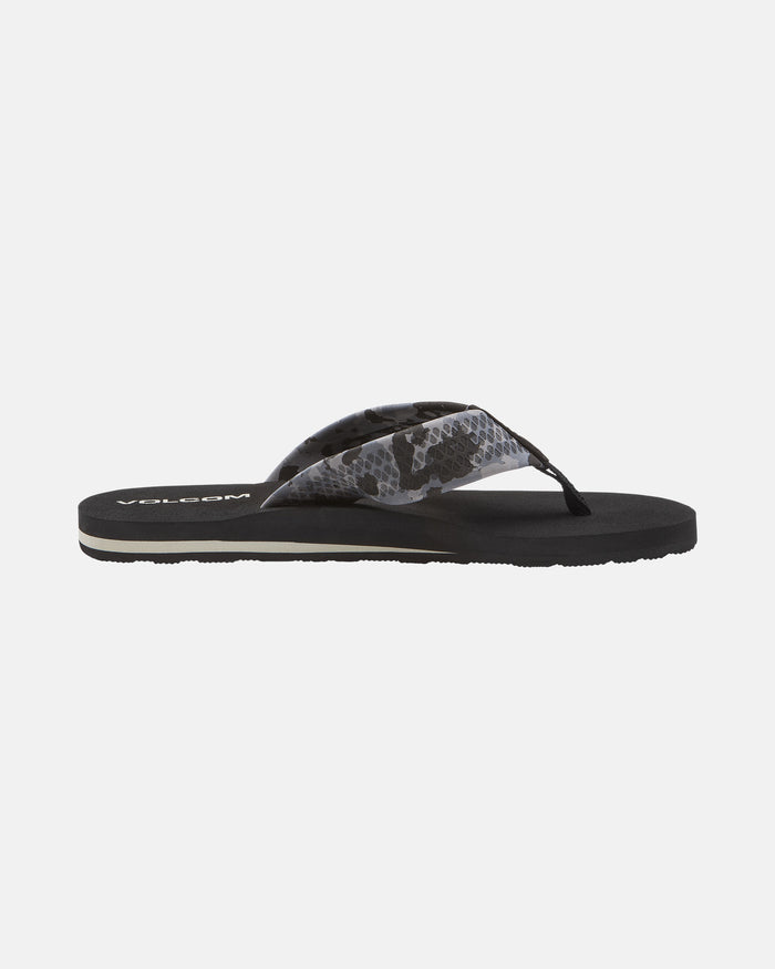 The Volcom Men's Daycation 2 sandal is a black flip-flop with a patterned grey and black fabric strap, cushioned EVA footbed, and molded rubber outsole, shown in side profile on a white background.