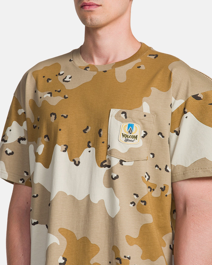 A man wears the Volcom Men's Desert Beers Pocket Short Sleeve Tee, a brown and beige camo heavyweight cotton shirt with a chest pocket and round Volcom Stone patch. Photo shows upper body from neck to mid-torso on a plain background.