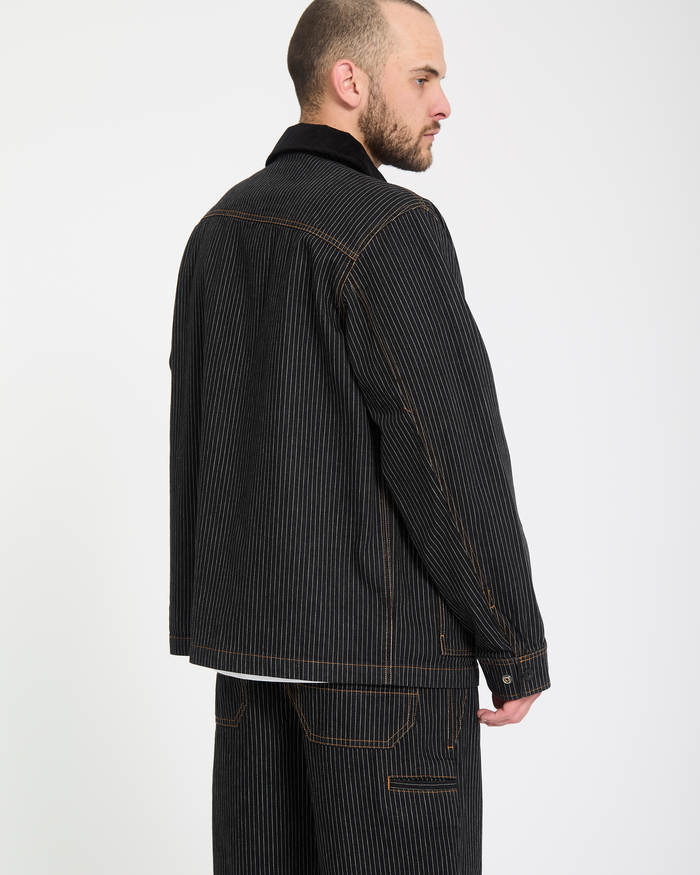 A man stands sideways against a white background, wearing Volcom Men's Dialed Work Pants featuring dark pinstripes and visible orange stitching.