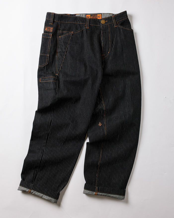 The Volcom Men's Dialed Work Pants feature black denim with white pinstripes, orange stitching, rolled cuffs, multiple pockets, and a metal waist button—combining durability and style for perfect workwear.