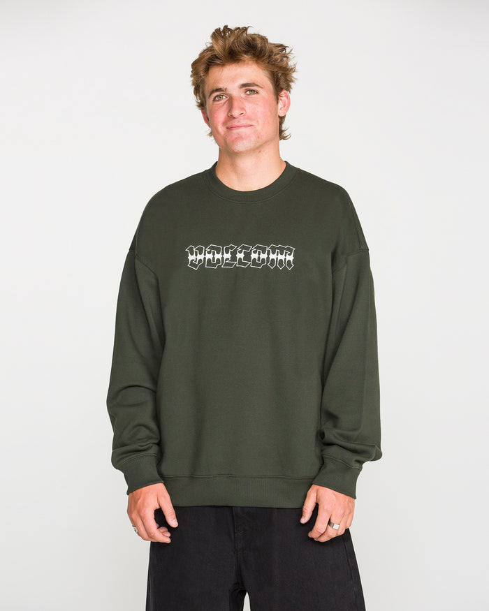 A person with short, tousled hair wears the Volcom Men's Dirty Work Crew— a green, loose fit fleece crew sweatshirt crafted from recycled polyester—paired with black pants and standing against a plain light background. The sweatshirt features white text for added style and offers both comfort and sustainability.