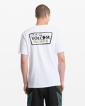 A man with short hair stands with his back to the camera, wearing Volcom’s Men's Dispatch Short Sleeve Tee in white, featuring a Hawaii license plate graphic on the back, paired with dark patterned shorts.