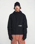 A man with a mustache, wearing a black beanie, black Volcom Men’s Double Insulated Jacket, black gloves, and light brown pants stands facing the camera against a plain white background.
