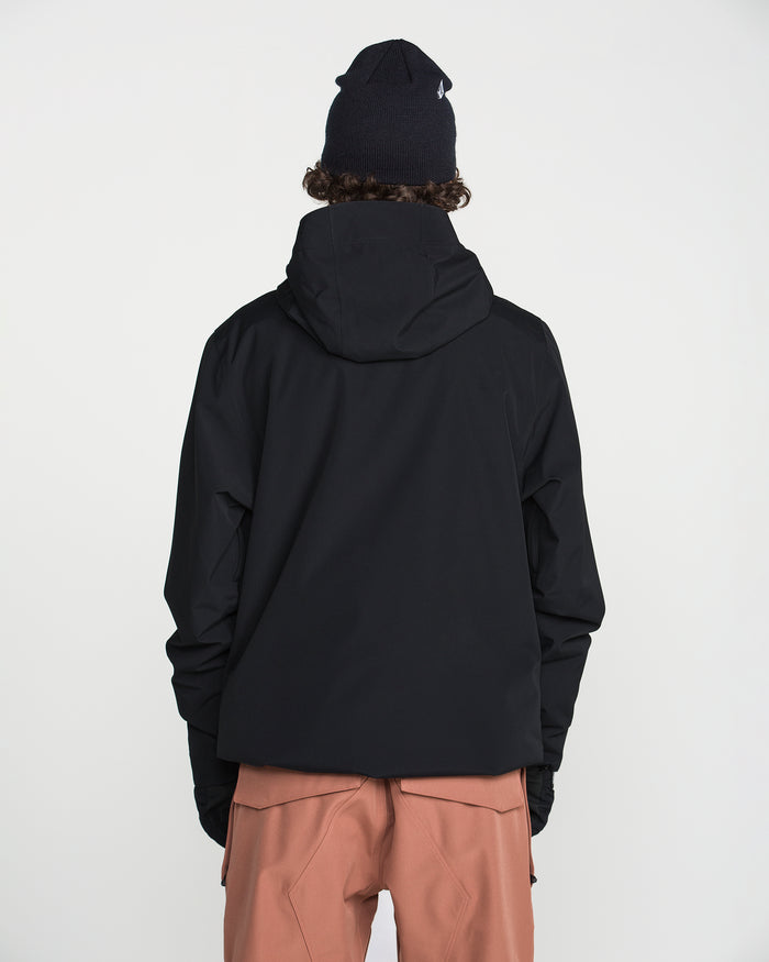 A person wearing the Volcom Men’s Double Insulated Jacket in black, paired with a black beanie and light brown pants, stands facing away from the camera against a plain white background.