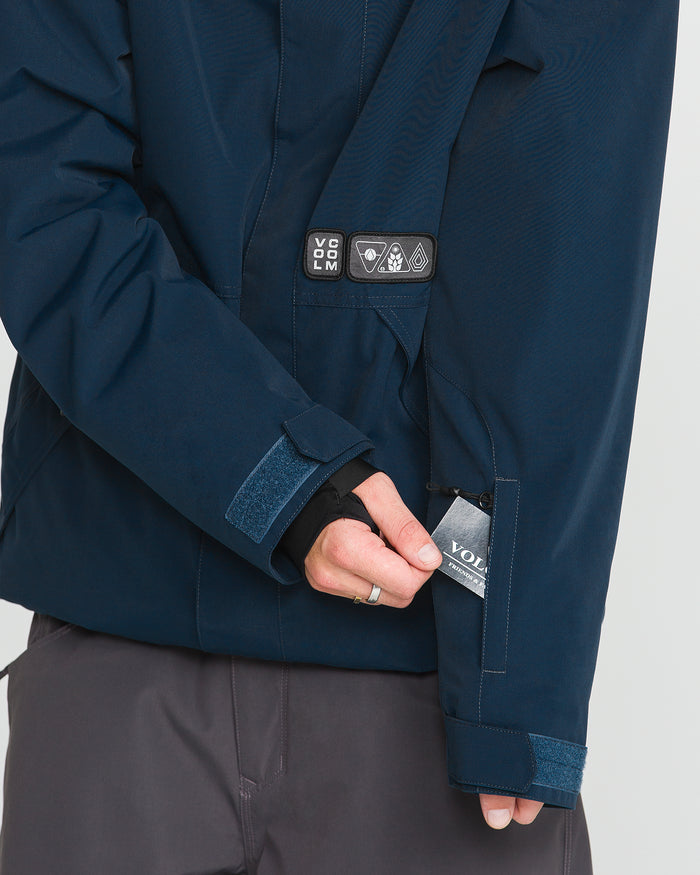 A person wearing the Volcom Men’s Double Insulated Jacket in dark blue and gray pants reveals the Volcom label from a small zippered pocket on the jacket sleeve.
