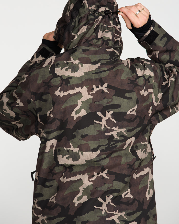 A person wearing the Volcom Men’s Double Insulated Jacket, featuring a 10K/10K V-Science camouflage pattern, stands facing away from the camera with the hood up and adjusts it with both hands.