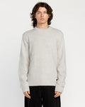 A man with wavy brown hair wears the Volcom Men's Edmonder II Sweater in light gray and loose black pants, standing facing forward against a plain white background.
