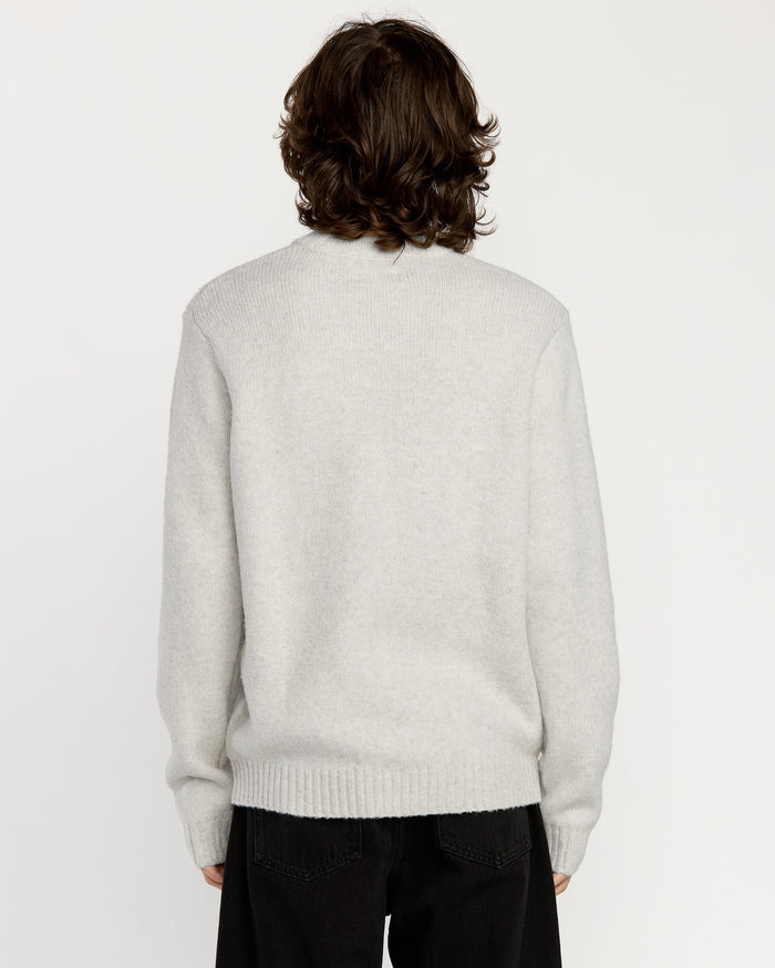 A person with medium-length brown hair is seen from behind, wearing the Volcom Men's Edmonder II Sweater in light gray with a crew neck, paired with black pants against a plain white background.