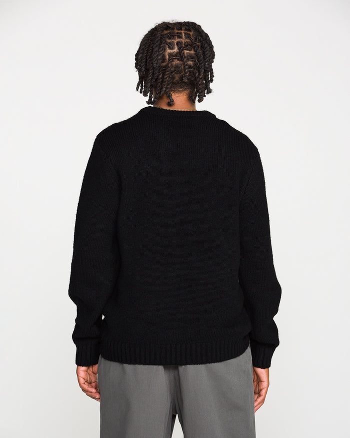 A person with braided hair stands facing away, wearing the Volcom Men's Edmonder II Sweater in black—crafted from recycled polyester—paired with gray pants, against a plain white background.