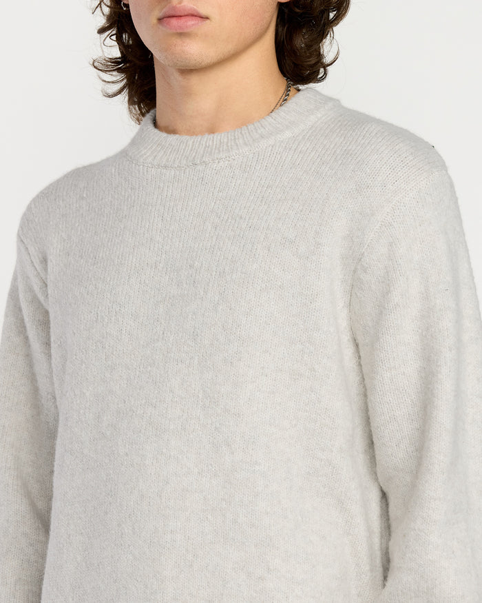A person with shoulder-length brown hair wears the Volcom Men's Edmonder II Sweater in light gray, made from recycled content, shown from shoulders to mid-torso against a plain white background with their face partially out of frame.