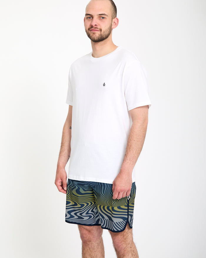 A man wears Volcom's Men's Encounter Scallop Mod 19 shorts and a white shirt.