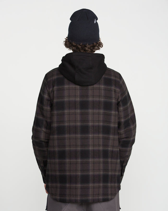 A person is standing with their back to the camera against a plain white background, wearing a black beanie, a fleece hood, and the Volcom Men’s Enson Insulated Riding Flannel.