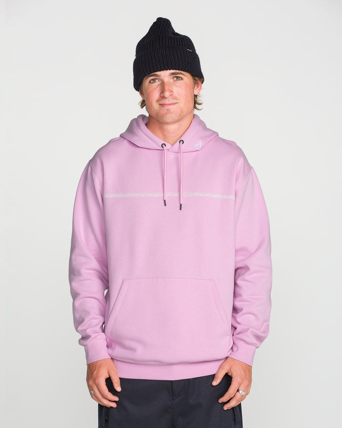 A person wearing a black knit beanie and the Volcom Men’s Essential Hoodie in light pink—crafted from soft cotton-poly fleece with a front pocket—stands facing forward against a plain white background, hands relaxed at their sides.