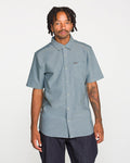A man with short dreadlocks and a tattooed arm wears the Volcom Men's Everett Oxford II Short Sleeve Shirt—a classic-fit, button-up style with a convenient front pocket, crafted from stretch-woven fabric for extra comfort. He stands against a plain white background.