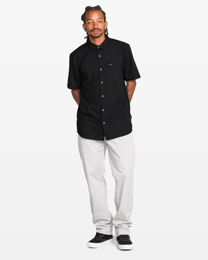 Man wearing a black button-up shirt and white pants on a white background