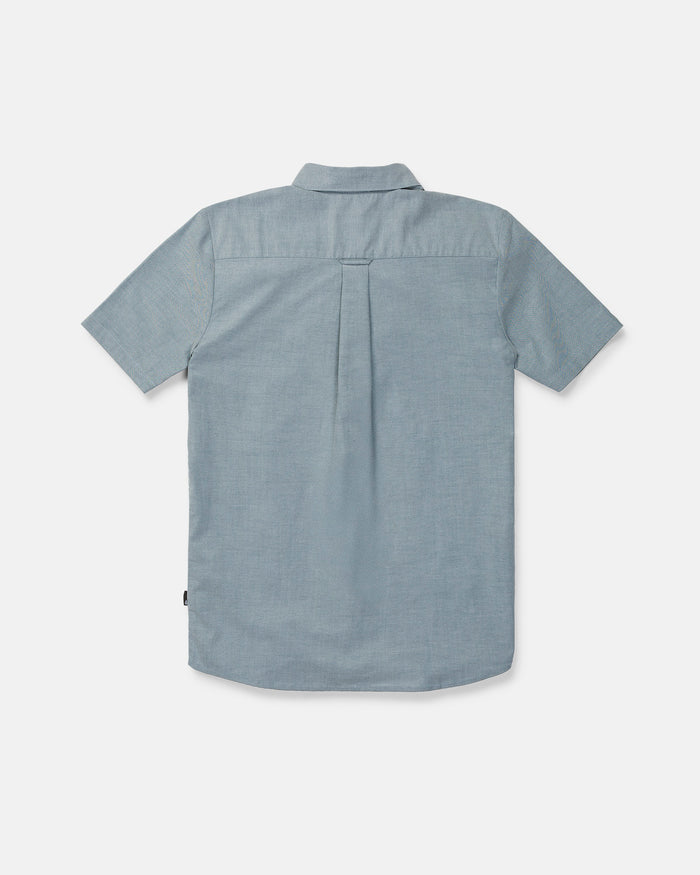 The Volcom Men's Everett Oxford II Short Sleeve Shirt is displayed from the back, highlighting its straight yoke, central pleat, and subtly curved hem. Crafted from lightweight, textured stretch-woven fabric for superior comfort, this classic fit button-up shirt is perfect for all-day wear.