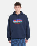 A person wearing the Men’s Featured Artist Antonio Carrau Pullover by Volcom—a navy blue heavyweight fleece hoodie adorned with a colorful graphic and text—stands against a plain white background. This Volcom hoodie includes a front pocket and is paired with blue checkered jeans.