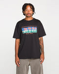 A man stands facing forward against a plain white background, wearing the Volcom Men's Featured Artist Antonio Carrau Short Sleeve Tee—a premium black shirt adorned with colorful graphics and the text "PRESERVING DISORDER SINCE 1991" and "Welcome Stone.