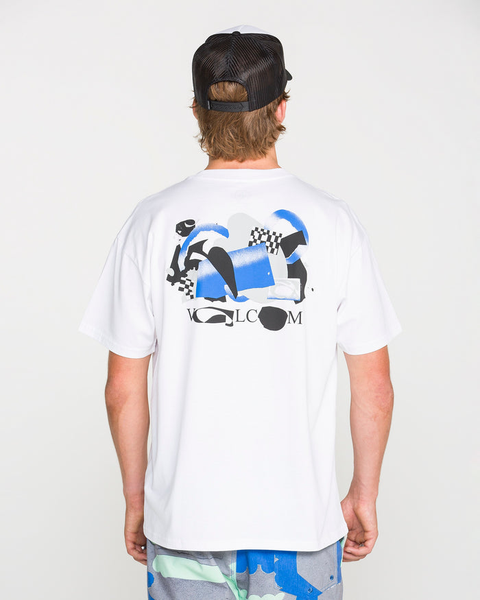 A person wearing the Volcom Men's Featured Artist Head Check Short Sleeve Tee in white, crafted from premium ringspun cotton and featuring abstract blue, black, and gray graphics with Antonio Carrau’s signature Volcom text on the back, paired with a black mesh cap and patterned shorts, stands against a plain background.