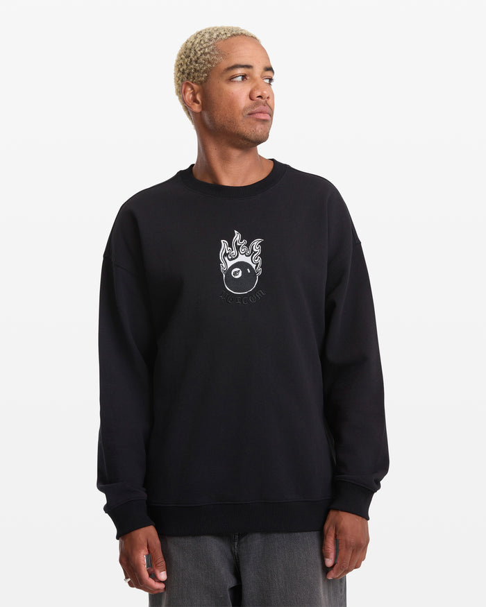 A person with short blonde hair models the Volcom Men's Featured Artist Seth Conboy Crew, a black fleece crewneck with small flaming yin-yang embroidery on the chest, standing against a plain white background and looking to the side.