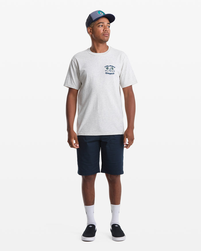 A man poses against a white background wearing the Volcom Men's Fed Up Short Sleeve Tee in gray, featuring a soft-hand screen print on the chest, paired with navy shorts, white socks, black sneakers, and a navy baseball cap.