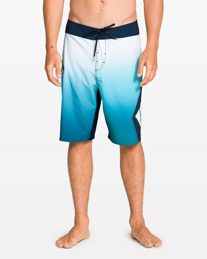 A person stands barefoot wearing Volcom Men's Foster Mod 21" boardshorts with Cinch Fly Technology, blue and white gradient design, cropped at chest to show the waist down against a light background.