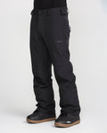 A person wearing black Volcom Men’s Freakin Snow Chino Pants and black winter boots with brown soles stands against a plain light background. The photo focuses on the lower half of the body, accentuating the men’s ski pants crafted from waterproof, breathable fabric by Volcom.