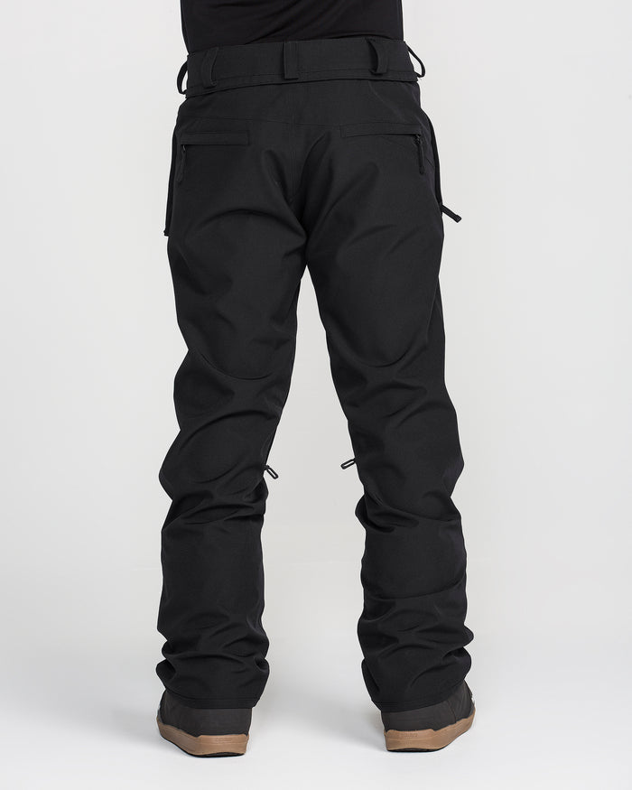 A person stands facing away, showcasing the Volcom Men’s Freakin Snow Chino Pants in black with brown boots against a plain white background. Only the lower body is visible, emphasizing the waterproof and breathable fabric of these men’s ski pants.