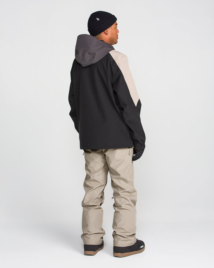 A person wearing a black and beige hooded jacket, Volcom Men’s Freakin Snow Chino Pants, gloves, and a black beanie stands facing away against a plain white background.