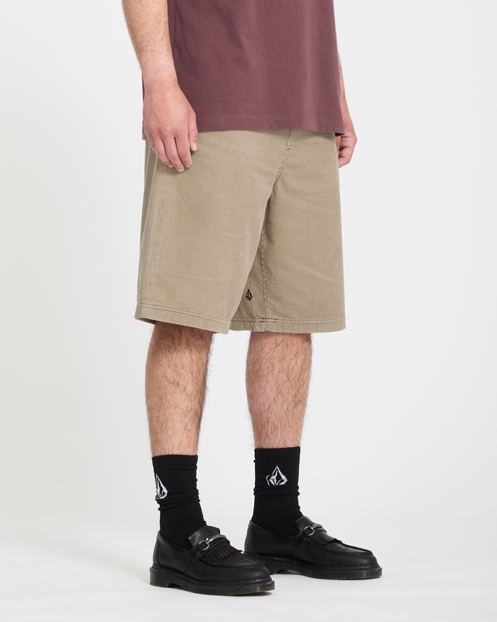 Wearing Volcom's Men's Freazy Loose Elastic Waist Short 22 in beige, paired with a maroon T-shirt, black socks with a white logo, and black loafers, a person stands against a plain white background—only their lower half is visible.
