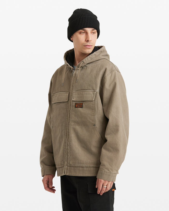 A man in a black knit beanie and the Volcom Men's Freshdust Workwear Jacket with large hand and chest pockets stands angled to the side, looking left against a plain white background.