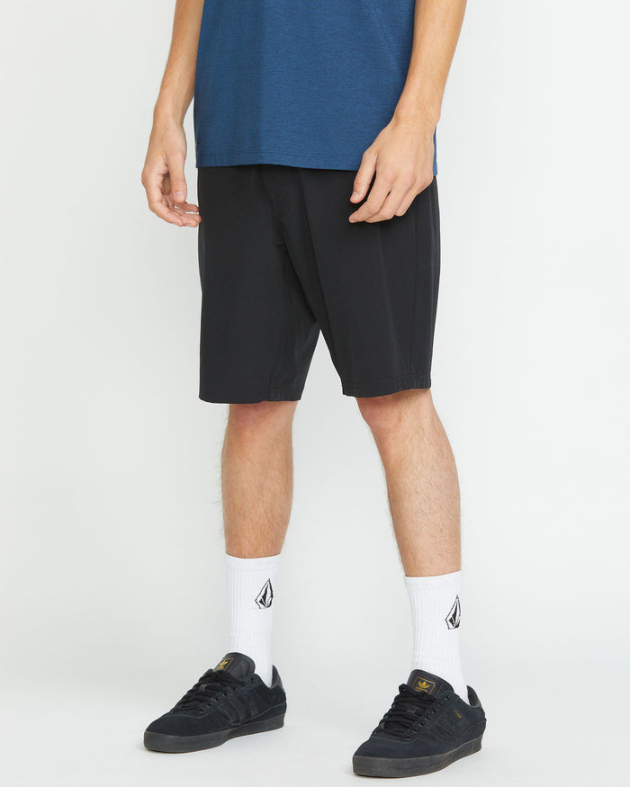 A person stands against a plain white background wearing a blue T-shirt, Volcom Men's Frickin Cross Shred 20" Shorts in black, white crew socks with a black logo, and black sneakers. The person's face is not visible.