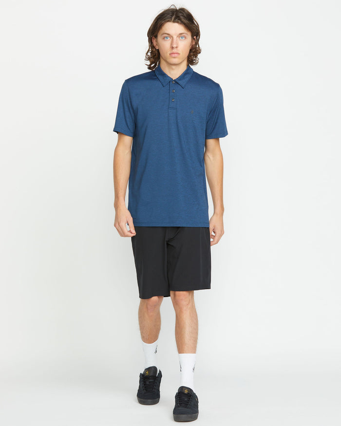 A person with long brown hair wears a dark blue polo and Volcom Men's Frickin Cross Shred 20" Shorts, paired with white socks and black shoes, standing against a plain white background.