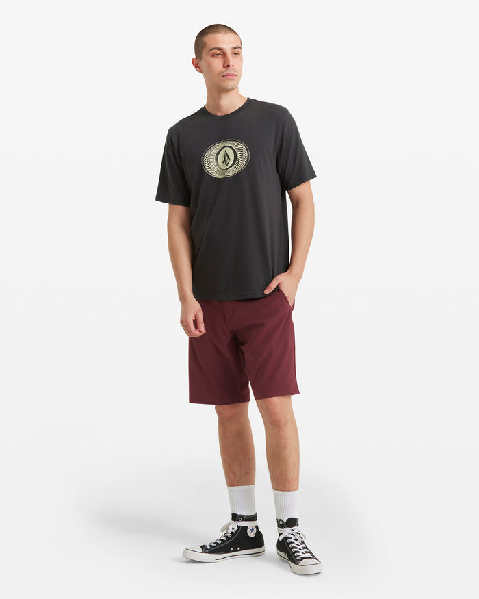A young man showcases classic Volcom style in a black graphic tee, white socks, black high-top sneakers, and maroon Men's Frickin Cross Shred Static Shorts by Volcom against a white background, one hand casually in his pocket as he looks to the side.
