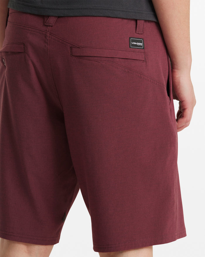 A person wears Volcom Men's Frickin Cross Shred Static Shorts in modern-fit burgundy, made from a recycled blend with back pockets and a black Volcom logo patch above the right pocket, standing against a white background.