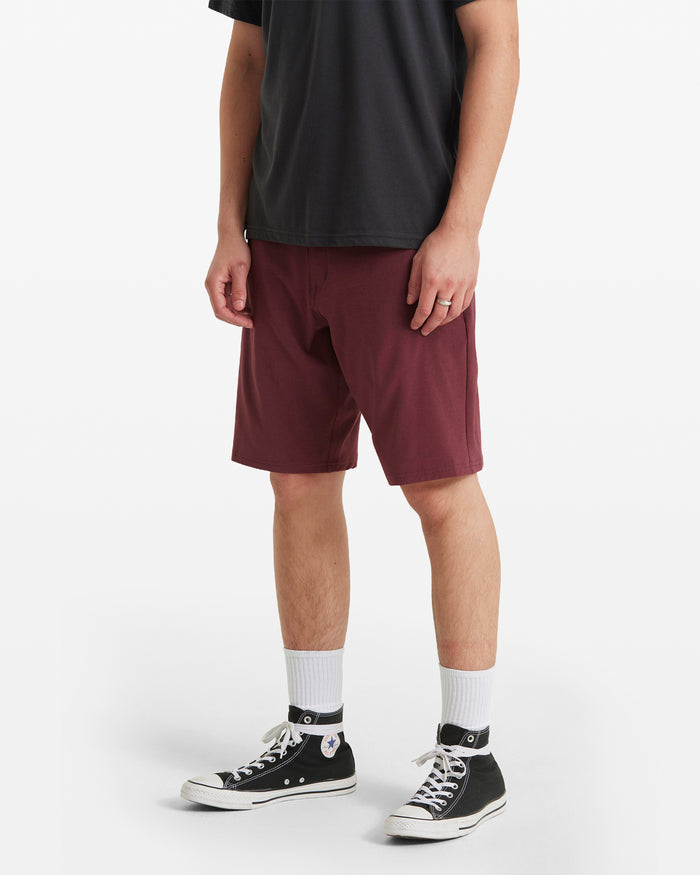 A person, shown from the shoulders down against a plain white background, wears black T-shirt, white socks, black low-top sneakers, and maroon Volcom Men's Frickin Cross Shred Static Shorts (modern fit, knee-length).