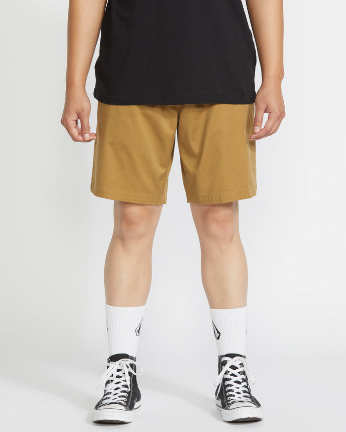 A person wears a black t-shirt, Volcom Men's Frickin Elastic Waist Shorts made with REPREVE fibers, white crew socks with a black logo, and black low-top sneakers, standing against a plain white background.