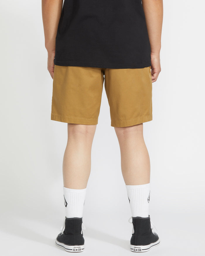 A person stands facing away from the camera wearing a black t-shirt, Volcom Men's Frickin Elastic Waist Shorts, white crew socks, and black sneakers against a plain white background.
