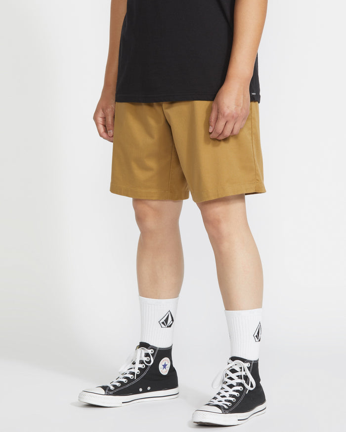 A person stands against a white background wearing a black t-shirt, Volcom Men's Frickin Elastic Waist Shorts made with REPREVE fibers, white diamond logo crew socks, and black high-top Converse sneakers.