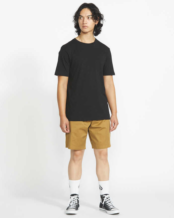 A person with medium-length curly hair wears a plain black tee, Volcom Men's Frickin Elastic Waist Shorts, white crew socks, and black high-top sneakers, standing against a white background.