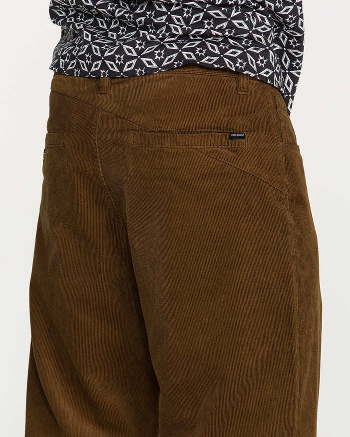 A person models the Volcom Men's Frickin Loose Tapered Cord pants in a Desert Palm shade, paired with a black-and-white patterned shirt. The cropped shot, spanning from chest to knees, highlights the rich texture and distinctive pocket details of these 100% cotton corduroy pants.