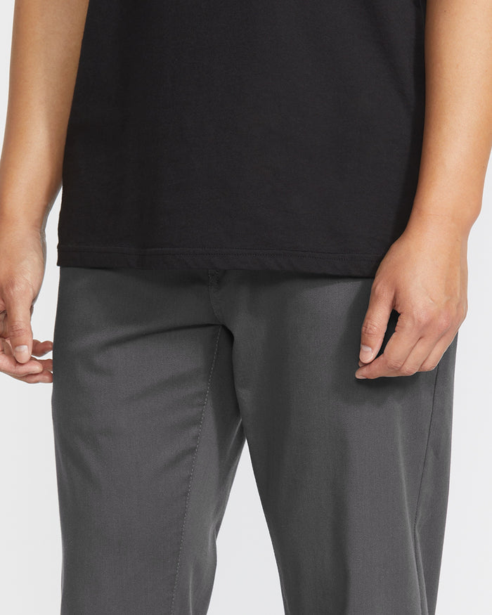 A person is shown from waist to mid-thigh wearing Volcom Men's Frickin Modern Stretch Pants in gray with a black shirt, arms relaxed at their sides against a plain background.
