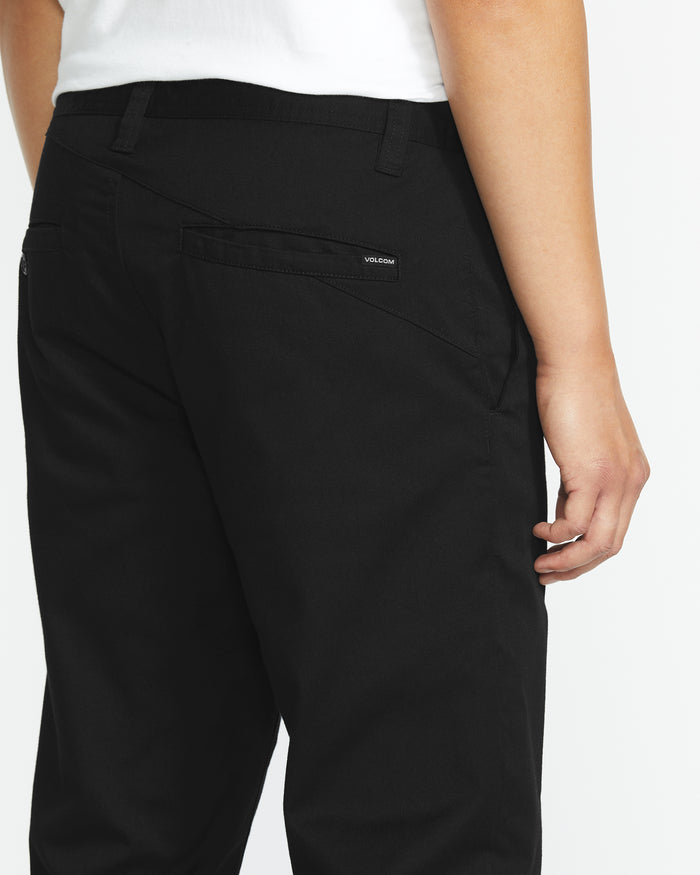 A man is seen from the back, highlighting the right side of his lower body in a white shirt and black Volcom Men's Frickin Modern Stretch Pants, which display a small Volcom label above the back pocket.
