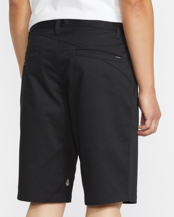 A person is shown from the back wearing a white shirt and black Volcom Men's Frickin Modern Stretch Shorts, featuring 5-pocket styling, back pockets, and a small Volcom logo near the hem.