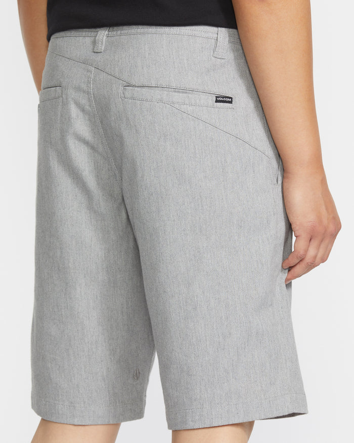 A man seen from behind wears light gray Volcom Men's Frickin Modern Stretch Shorts with back pockets and a small black logo tag above the right pocket. These cotton stretch shorts offer comfort and style.