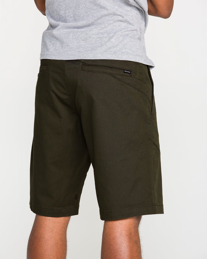 A person wearing a gray T-shirt and dark green Volcom Men's Frickin Modern Stretch Shorts is standing with their back to the camera. Only the lower torso and upper legs are visible against a plain background, emphasizing the breathable fabric of these Volcom shorts.
