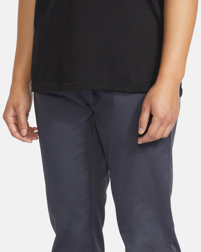 A person is shown from shoulders to knees, wearing a black shirt and Volcom Men's Frickin Slim Joggers in dark gray made with REPREVE recycled fibers, standing with arms relaxed against a plain background.