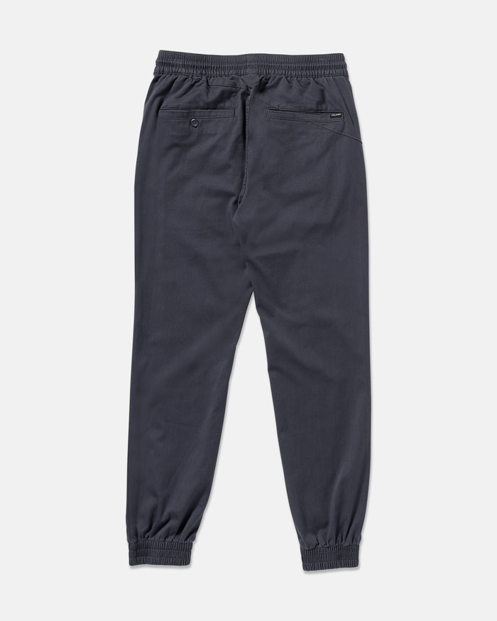 The Volcom Men's Frickin Slim Joggers in dark gray are shown from the back, featuring an elastic waistband, slim fit, two back pockets (one with a button), and made from REPREVE recycled fibers on a plain white background.